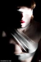 Blindfolded woman in bandages with red lips. Light painted photograph.